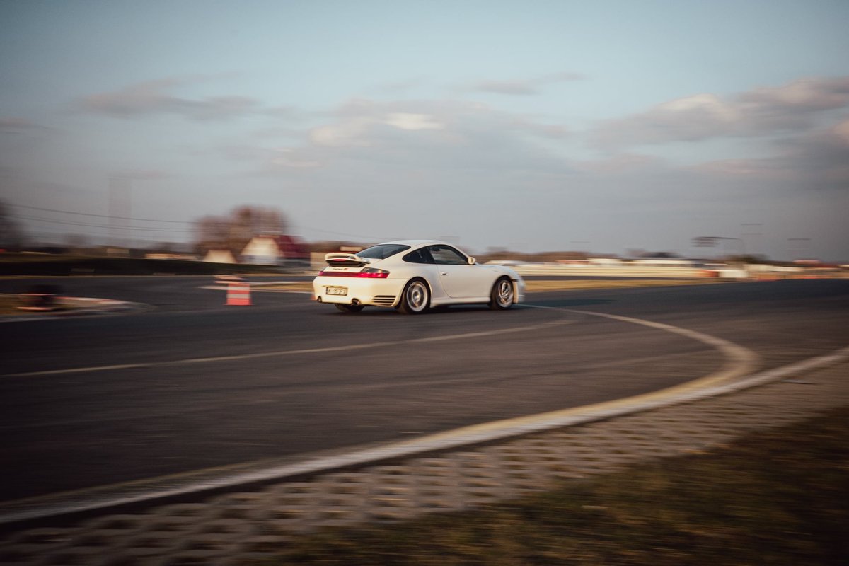 White Porsche 996.2 rear view pulling away on track at sunset with cobblestone run-off