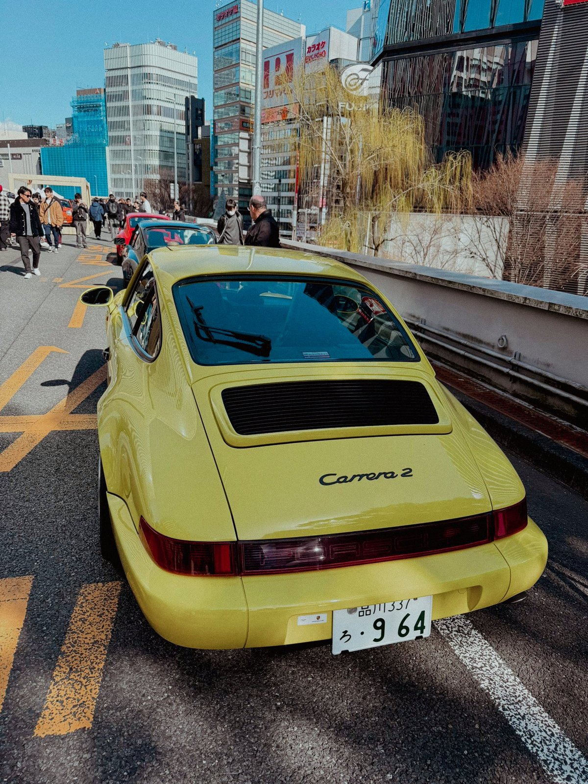 Yellow Porsche 964 Carrera 2 rear view on the expressway with Ginza buildings behind