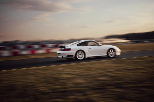 White Porsche 996.2 rear three-quarter rolling shot with barriers in background at dusk