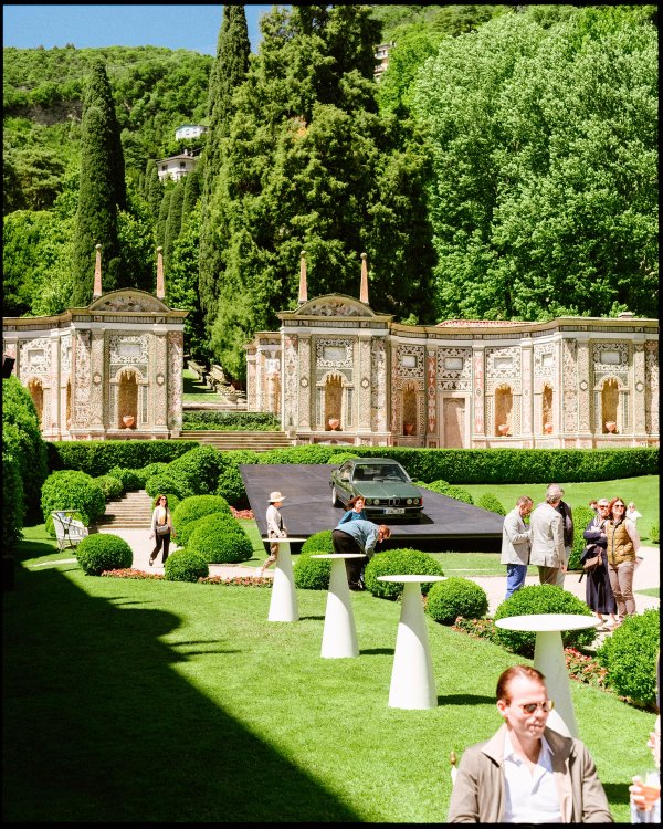 Pre-war BMW roadster on a raised stage in the villa garden, surrounded by an audience in formal dress