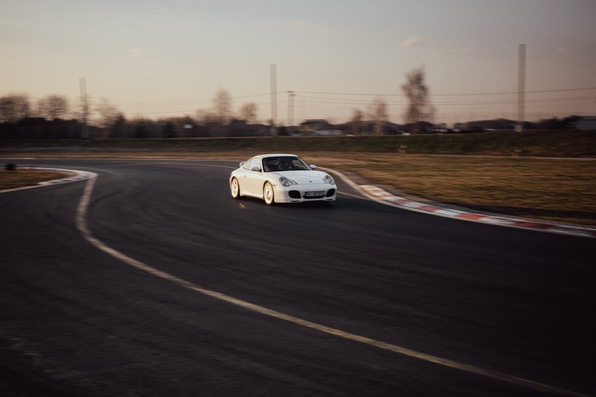 White Porsche 996.2 coming through a corner on track with motion blur at sunset