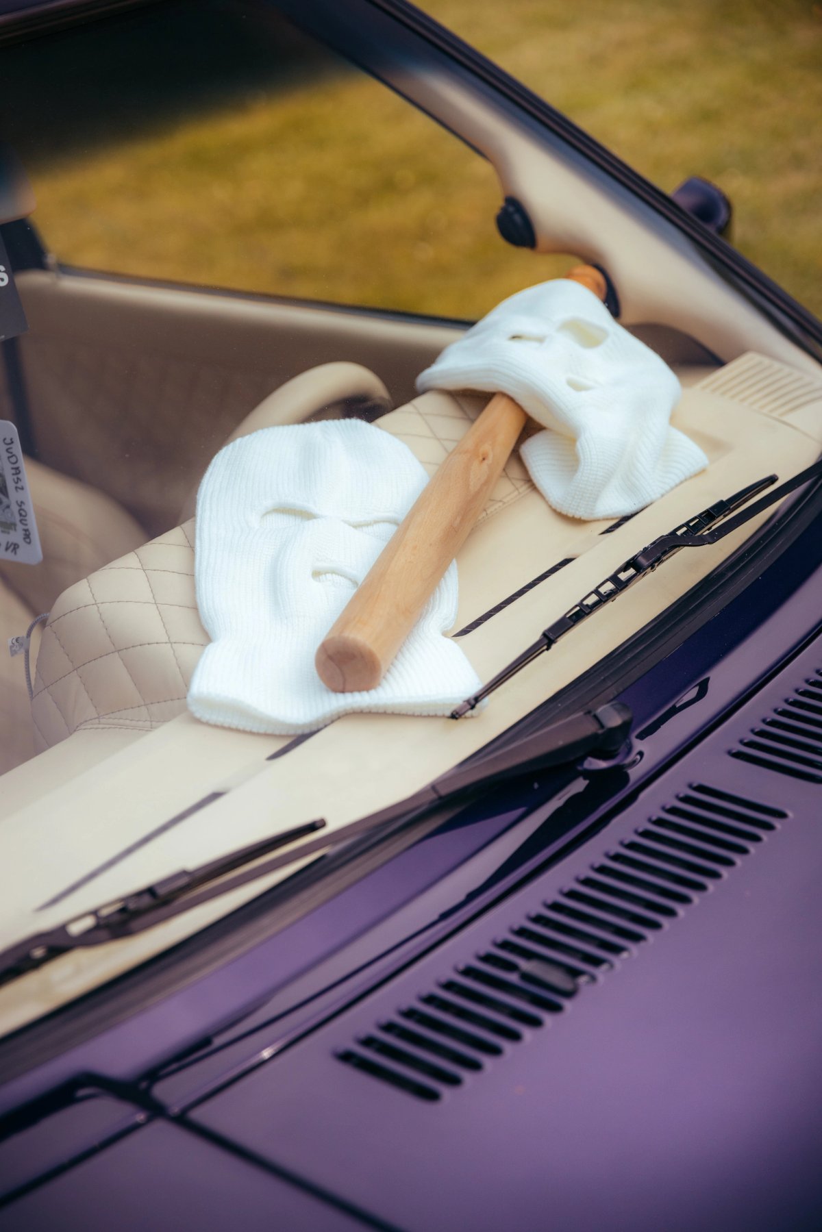 White balaclavas and a cigar on the dashboard of a purple car seen through windshield