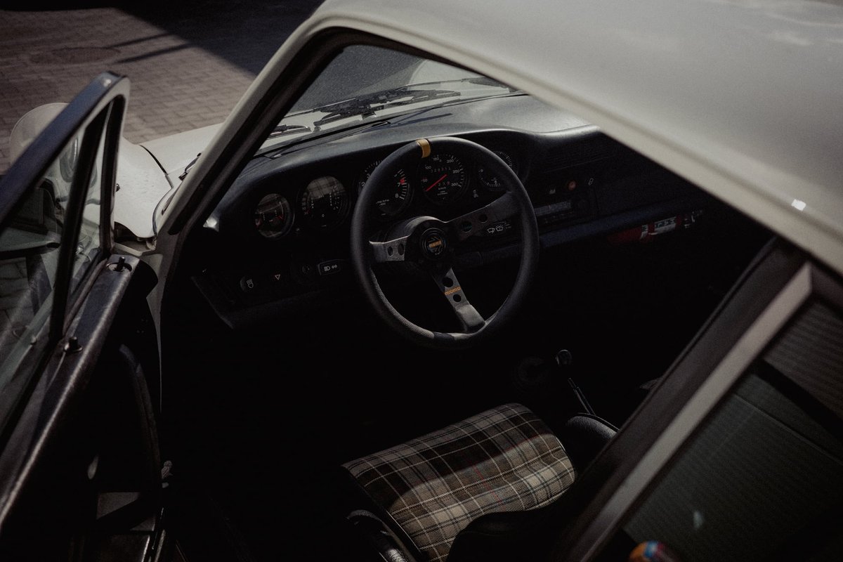 Interior of white Porsche 911 G-series showing tartan sport seats and thin steering wheel