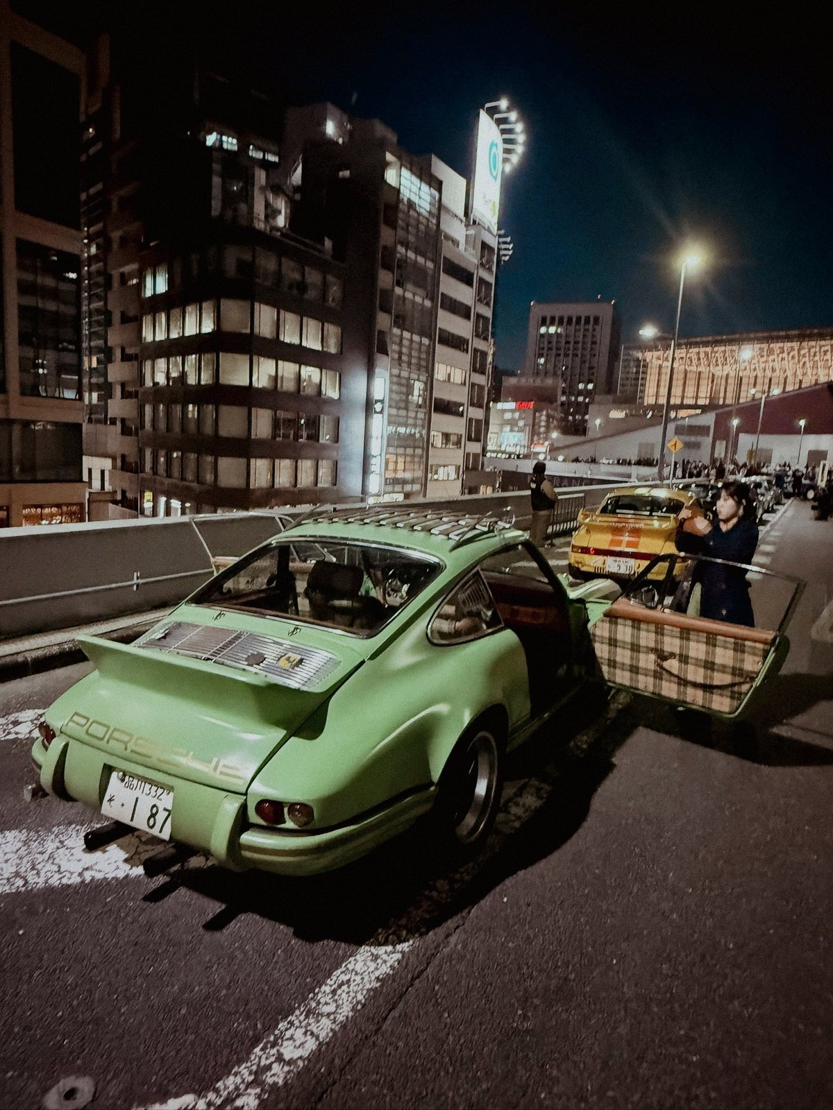 Green early Porsche 911 rear at night on Tokyo street with roof rack and plaid blanket