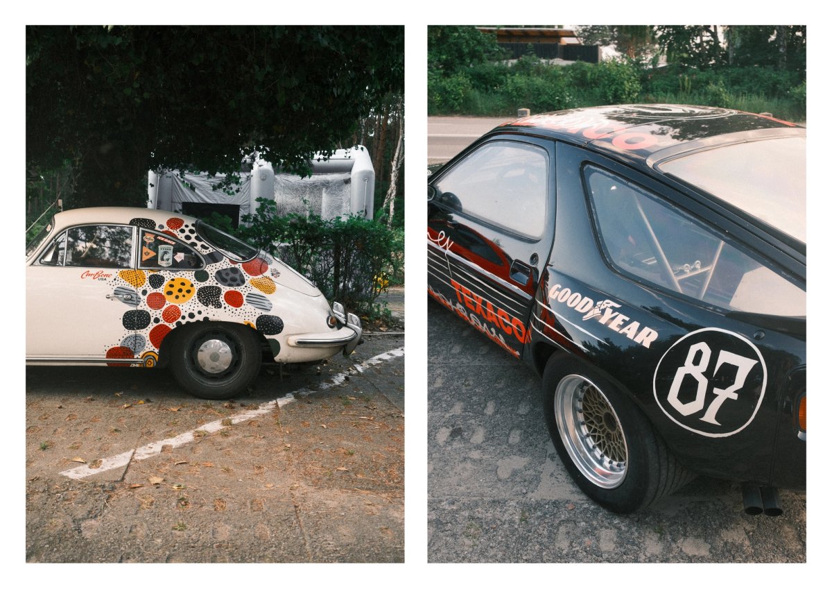 A cream Porsche 356 in a colourful polka-dot art livery beside a black Porsche 928 race car number 87 in Goodyear livery