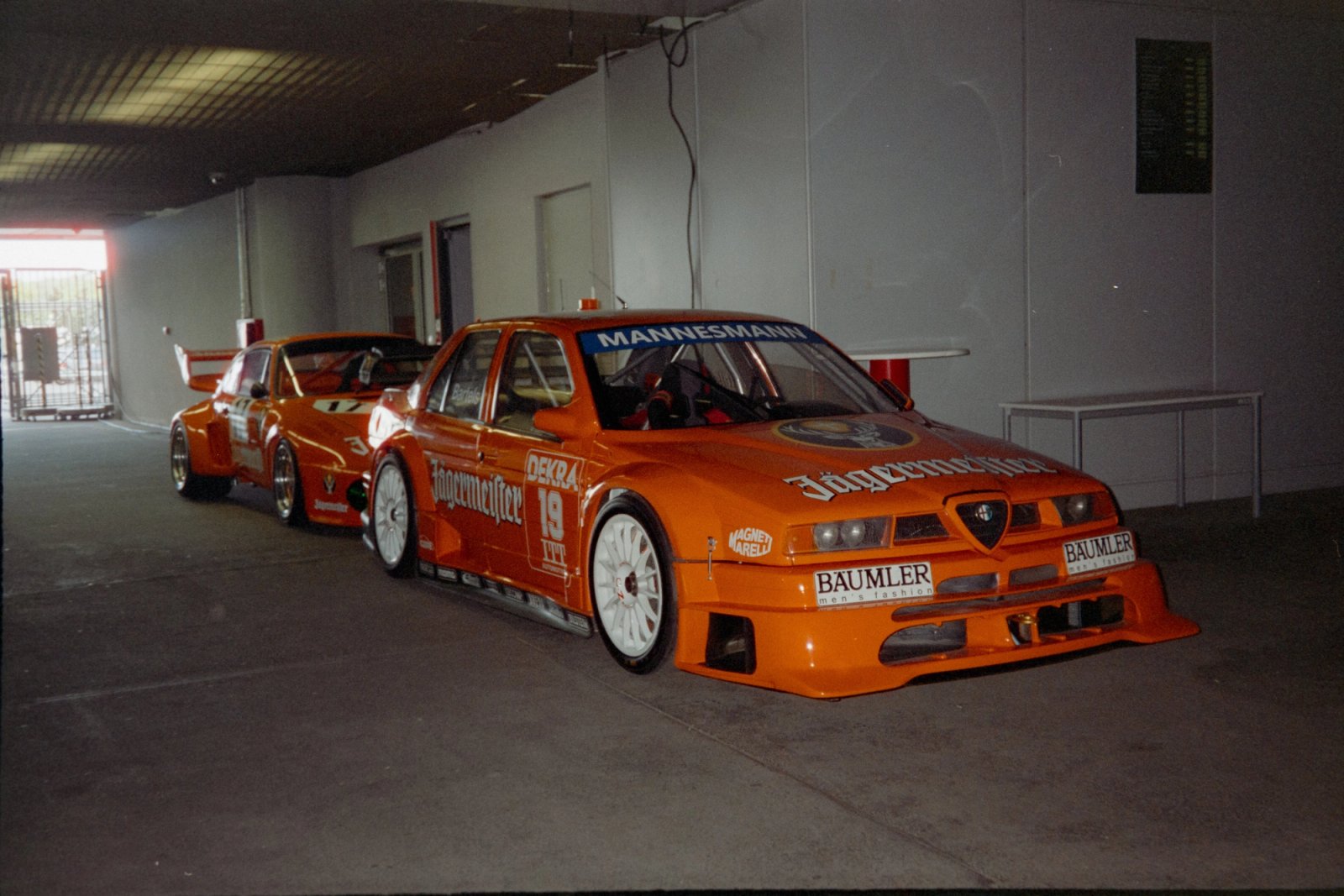 Two Jägermeister orange DTM race cars, Alfa Romeo 155 V6 TI, side by side in the paddock garage