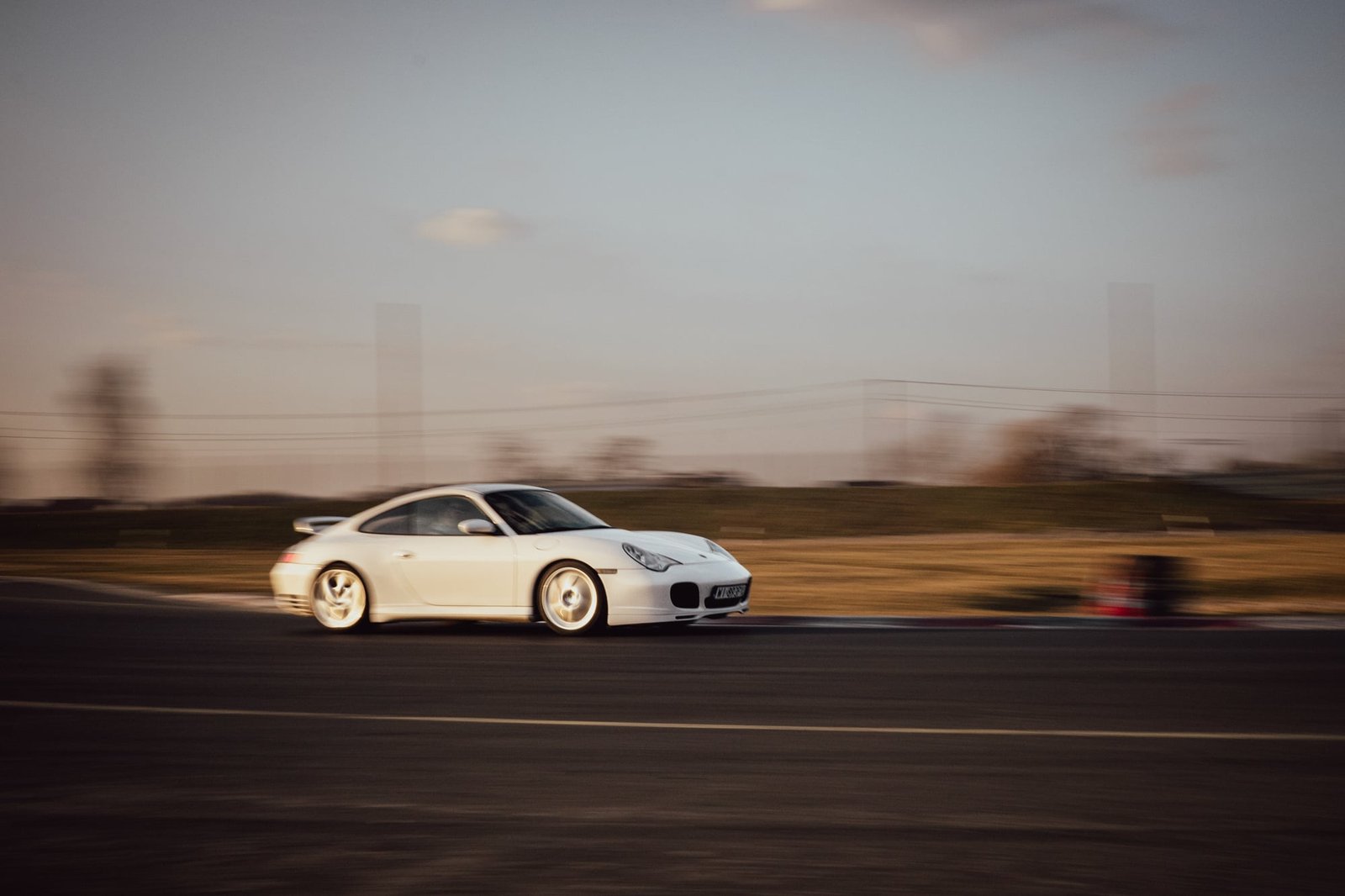 White Porsche 996.2 side profile rolling shot on open track at golden hour