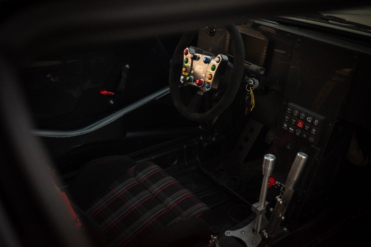 Rally cockpit with ECU Master button plate on the steering wheel, carbon dashboard, tartan Recaro seat, and hydraulic handbrake