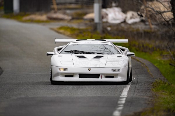 White Lamborghini Diablo driving on a Japanese country road with headlights on