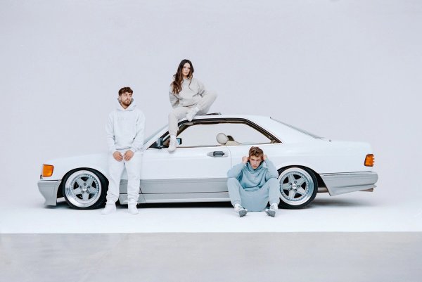 Three models with a white Mercedes SEC AMG on white cyclorama