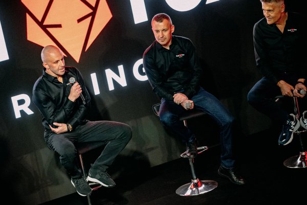 Three men on stage at the Red Fox Racing launch event with microphones