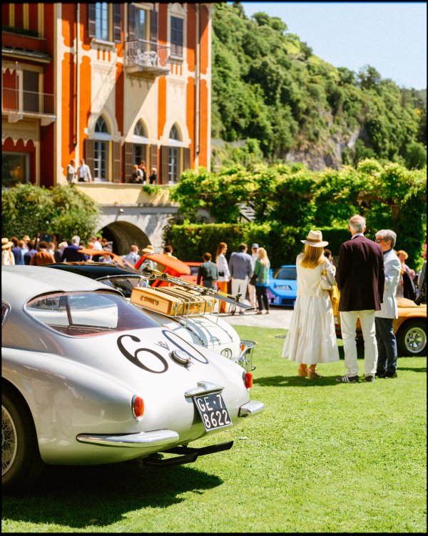 Rear three-quarter of silver vintage racing coupé number sixty with red ochre villa and guests in linen and hats