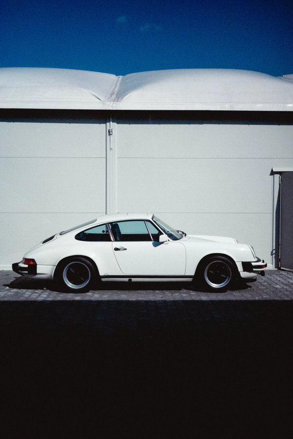White Porsche 911 G-series Carrera 3.0 side profile with black Fuchs wheels against garage door