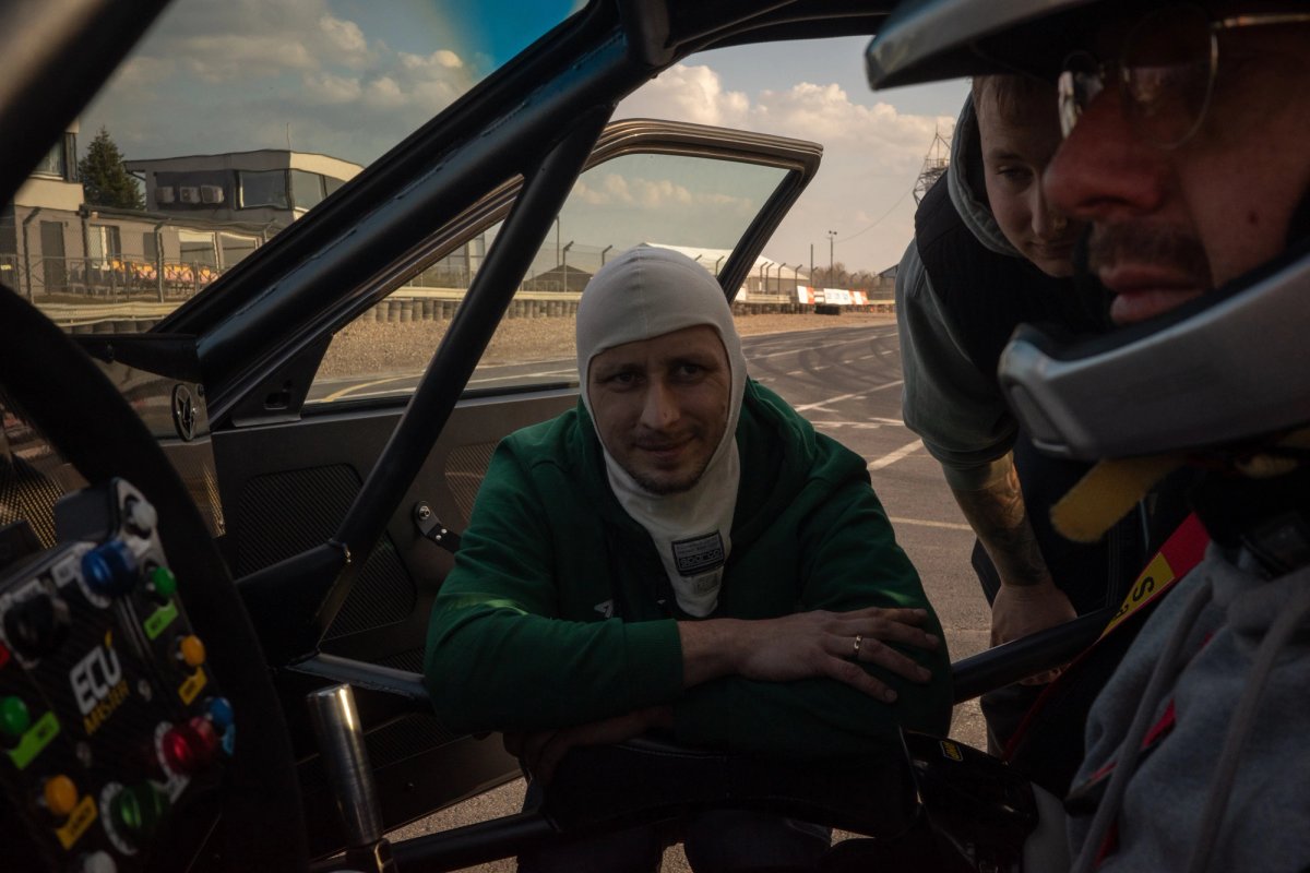 Driver in balaclava and green jacket talking to a mechanic through the roll cage before the first run