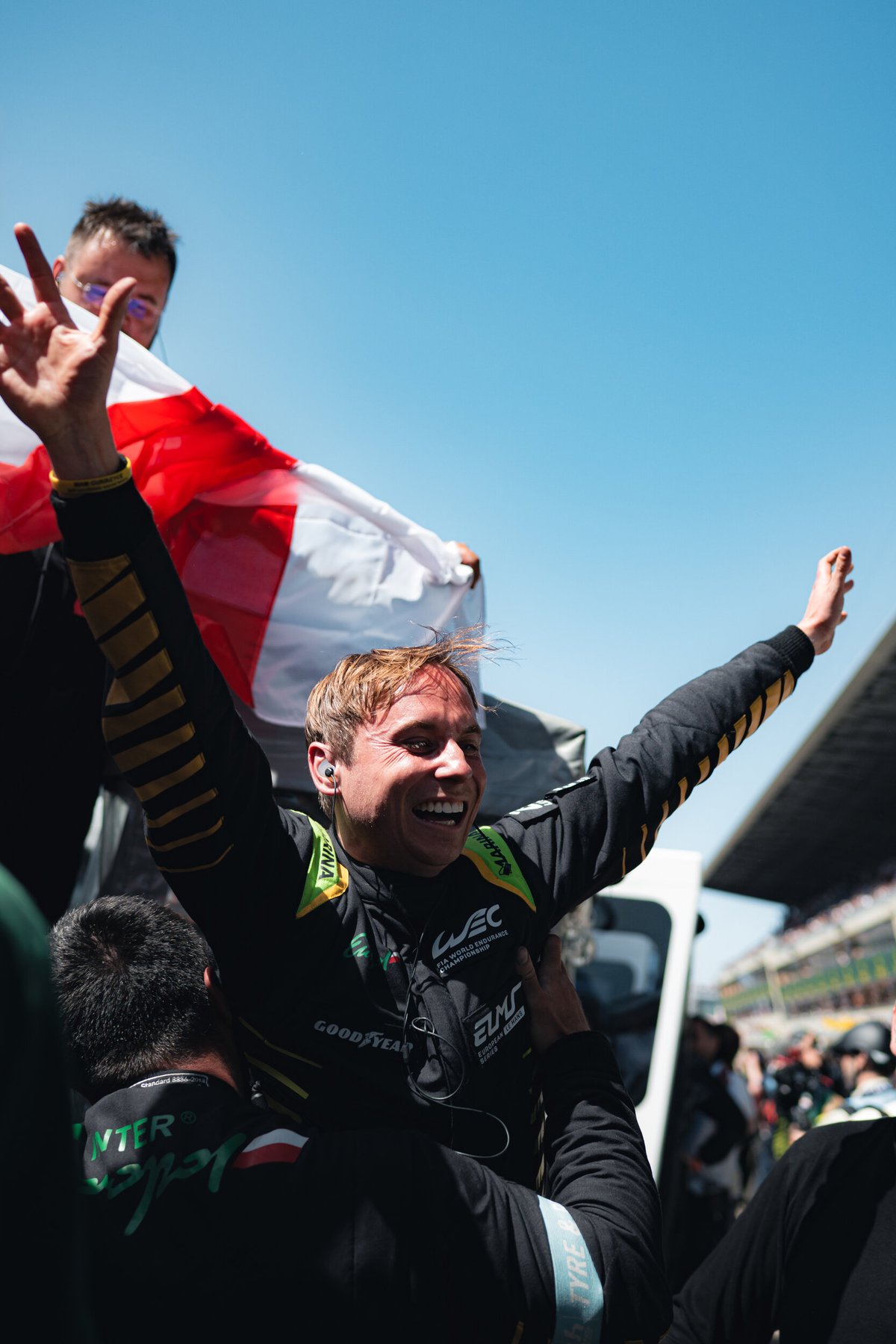 Inter Europol Competition driver lifted by the crew in celebration, arms raised, a Polish flag held up behind under a blue sky