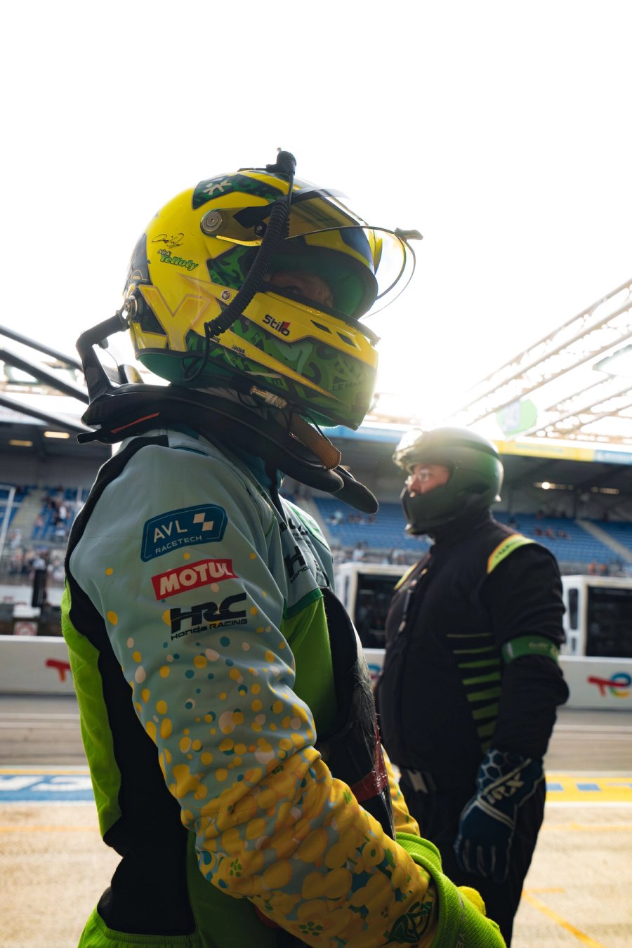 Inter Europol driver in the pit lane in golden morning light, in the rapeseed-pattern race suit and helmet