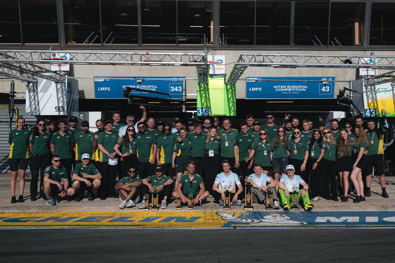 The full Inter Europol Competition team posing with their trophies in the Le Mans pit lane beneath the 43 and 343 pit boards after the LMP2 one–two