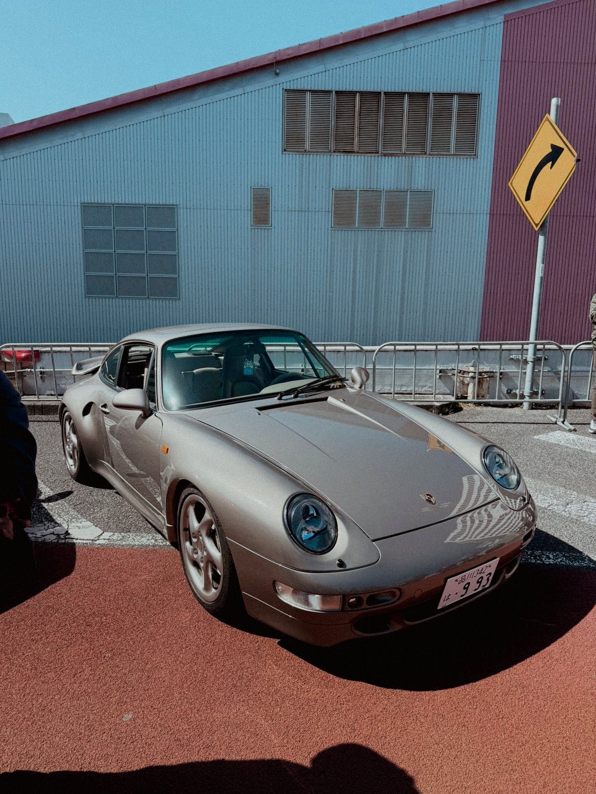 Silver Porsche 993 front view with yellow road sign and industrial building behind