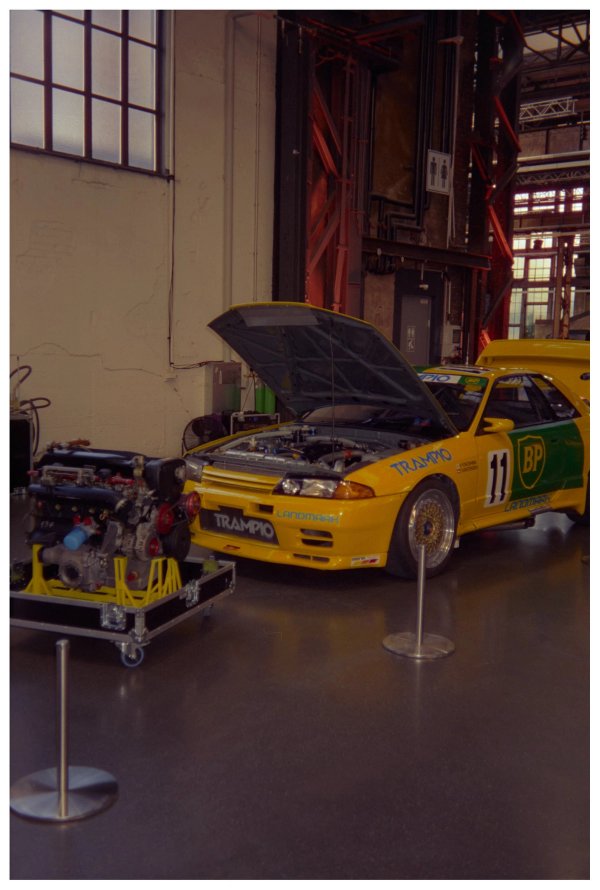 Yellow Trampio Nissan Skyline GT-R R32 with number 11 and BP Oil livery, hood open showing the engine bay, with a separate RB26 engine on a stand next to it