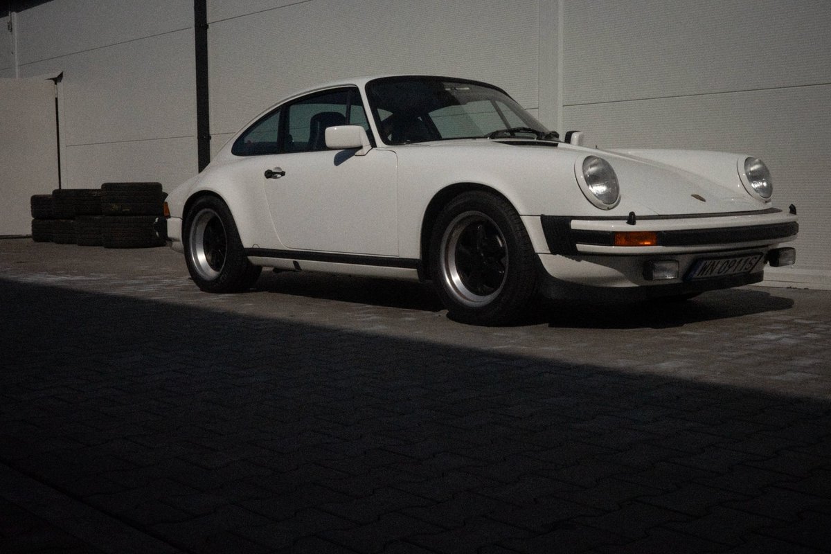 White Porsche 911 G-series Carrera 3.0 front three-quarter view with black Fuchs wheels at dusk