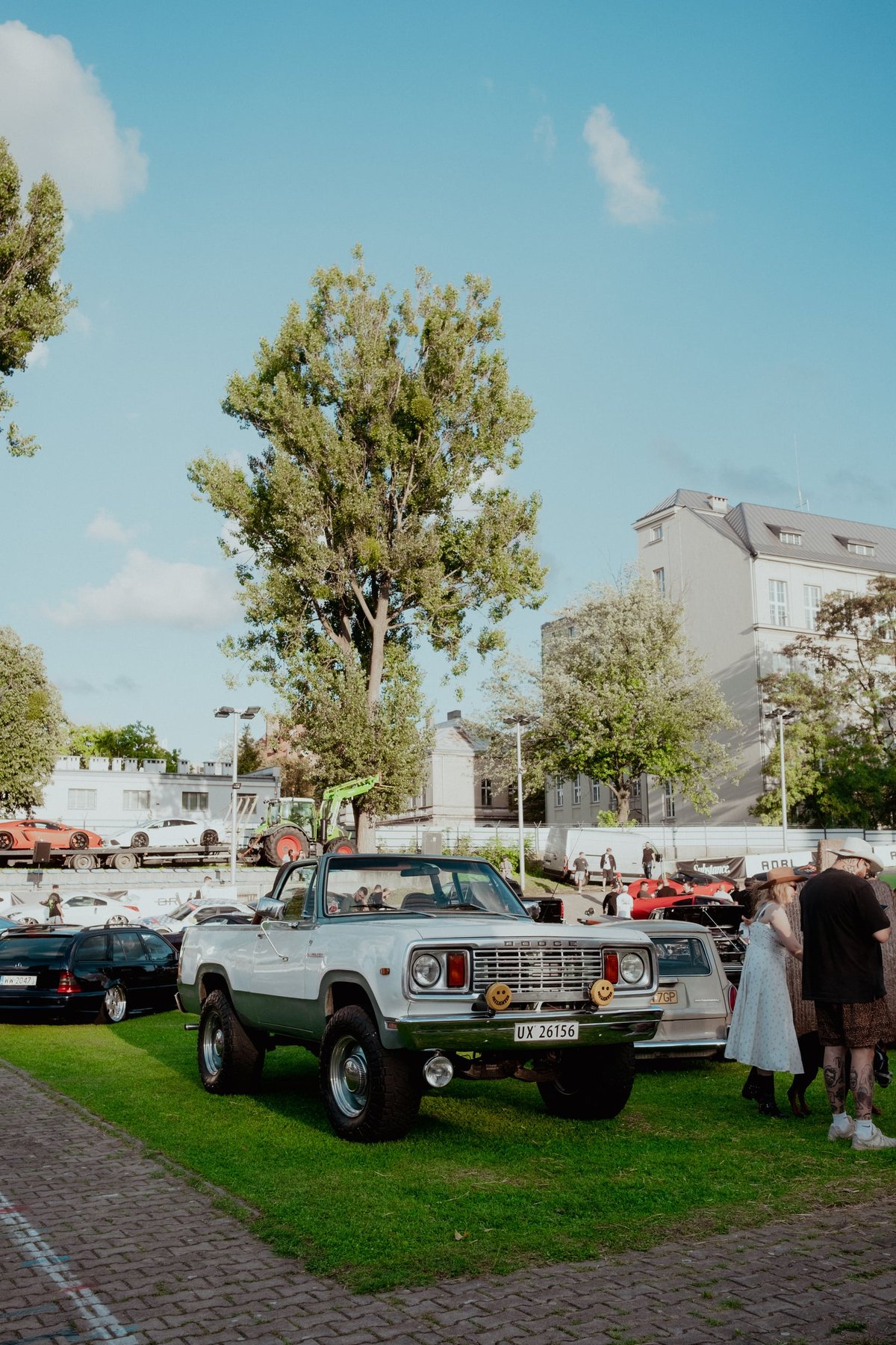 An open-top Dodge Ramcharger parked on the grass inside the Łódź velodrome, with a car transporter and a poplar tree behind it