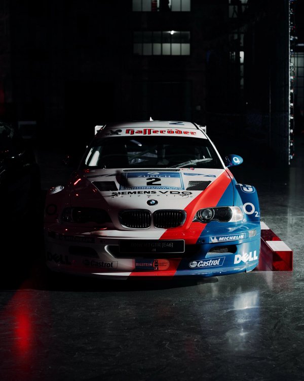 BMW M3 GTR E46 race car in Hasseröder white, blue and red livery with number 2, lit dramatically from above in a dark hall
