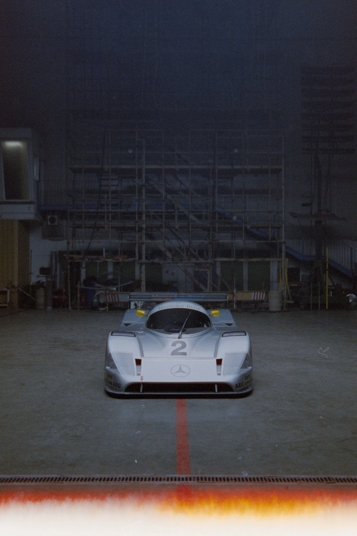 Mercedes Sauber C11 head-on from a distance with red line on floor and scaffolding behind