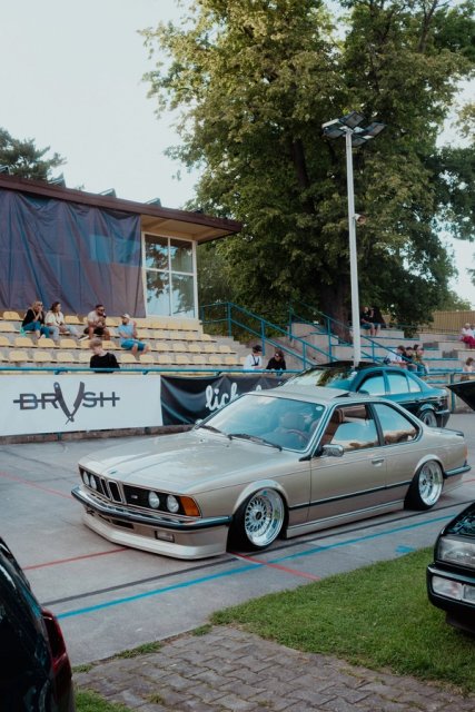 A silver BMW 6 Series E24 on the concrete of the velodrome, empty grandstand behind