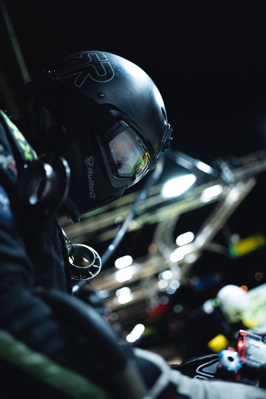 Inter Europol crew member in a dark helmet leaning over the car during a night pit stop, lit by the pit lights