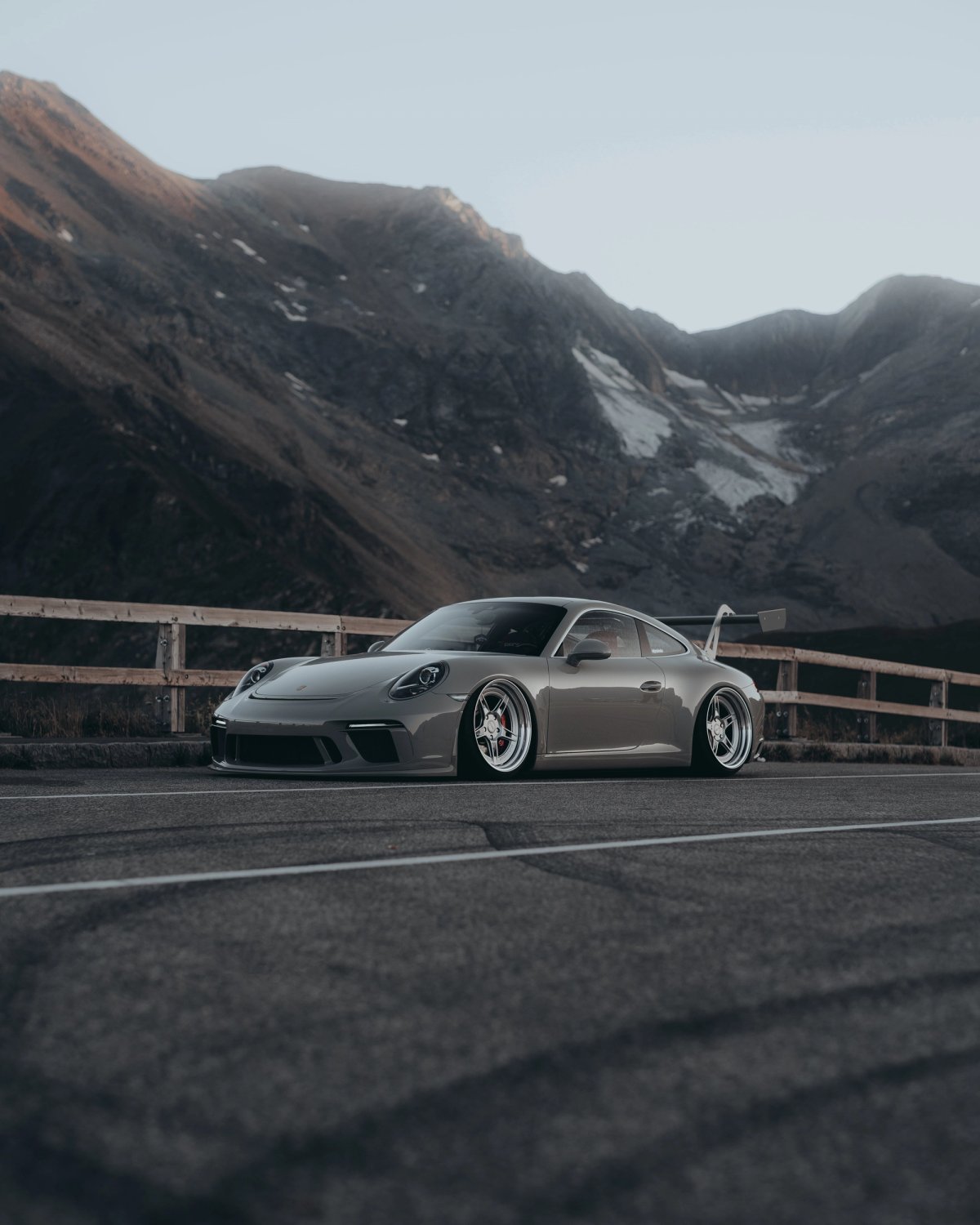 Lowered Porsche 991 on an alpine pass with wooden fence and brown mountains