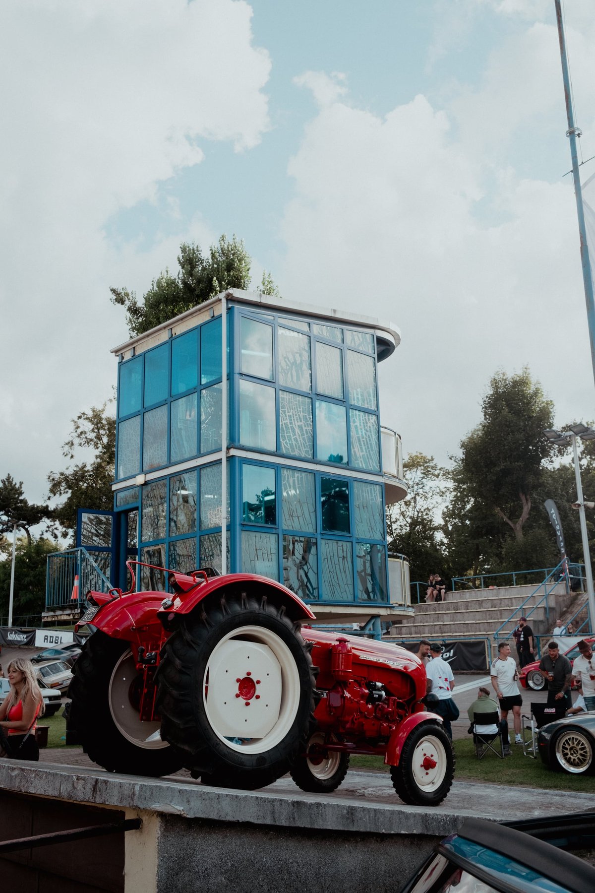 A red Porsche Diesel tractor parked below the glass timing tower of the Łódź velodrome