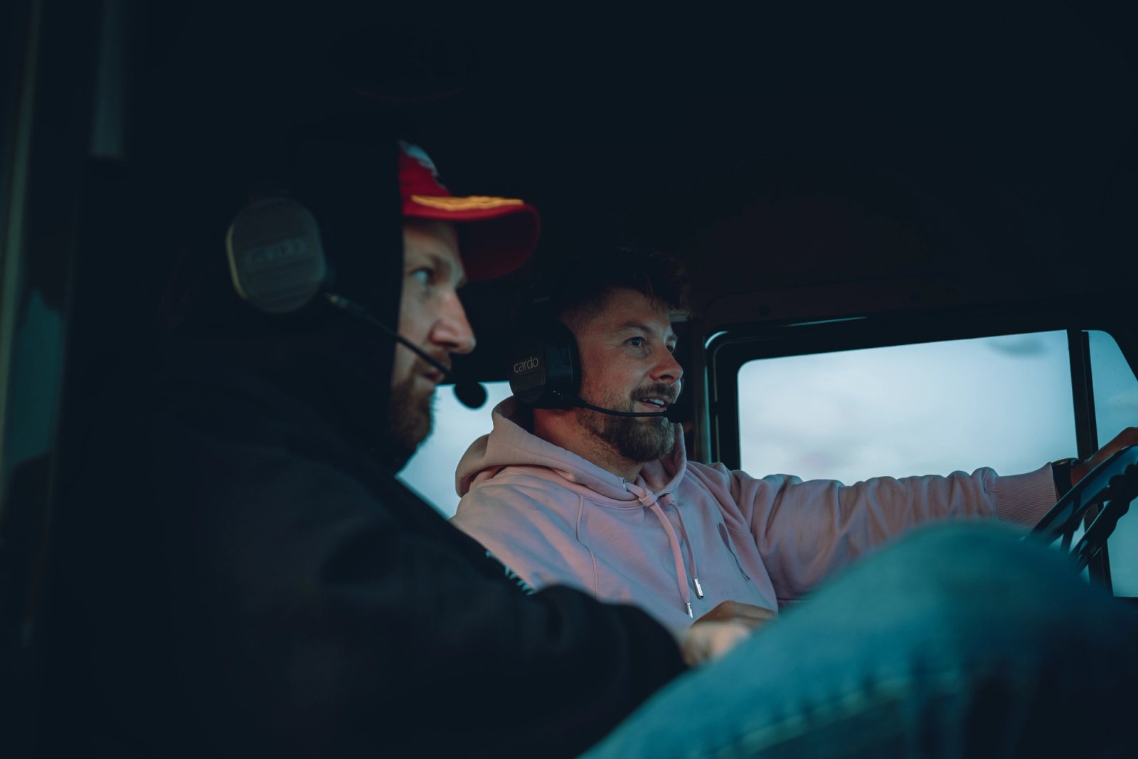 Daniel and Michał inside the Unimog cab wearing Cardo headsets, eyes on the road