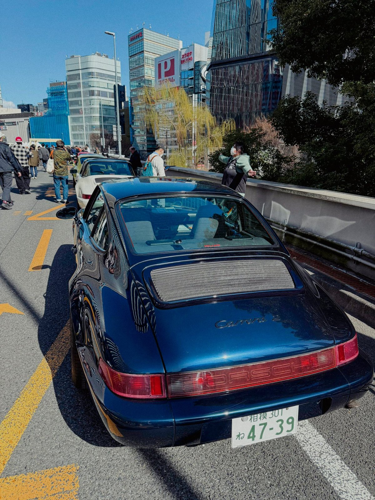 Blue Porsche 964 Carrera 2 rear view on the expressway with Ginza buildings and crowd