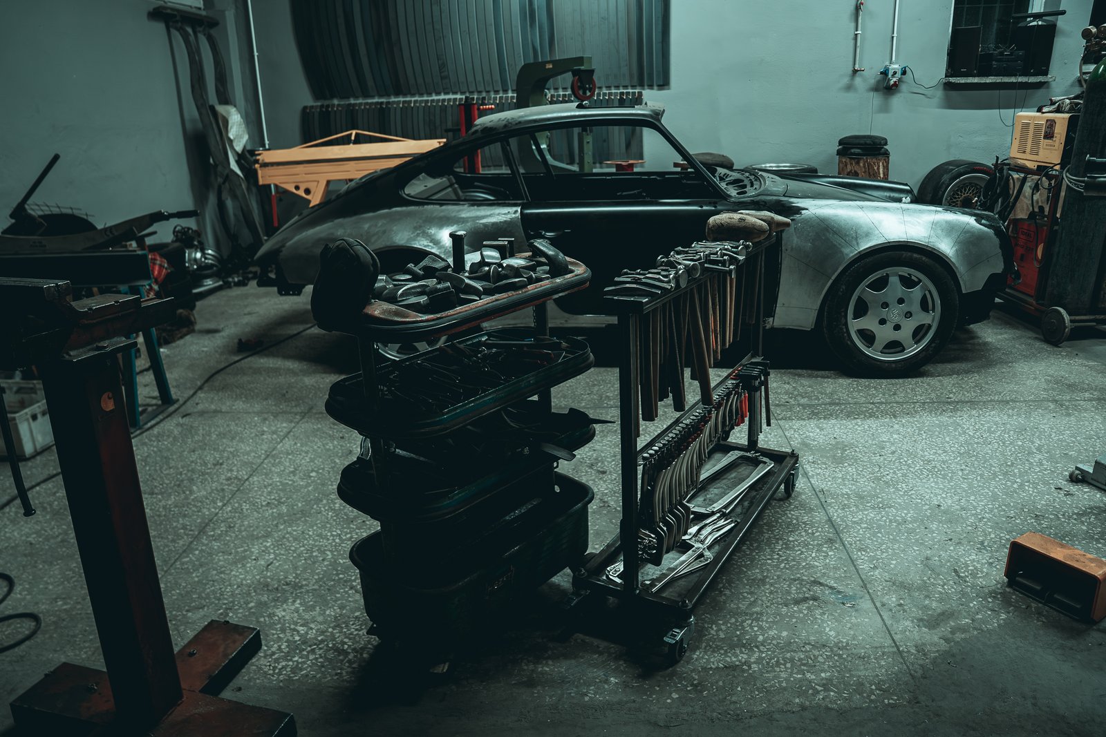 Porsche 911 in bare metal in the 1991Rework workshop with a loaded tool cart