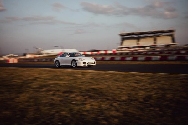 White Porsche 996.2 front three-quarter on track with grandstand and barriers behind