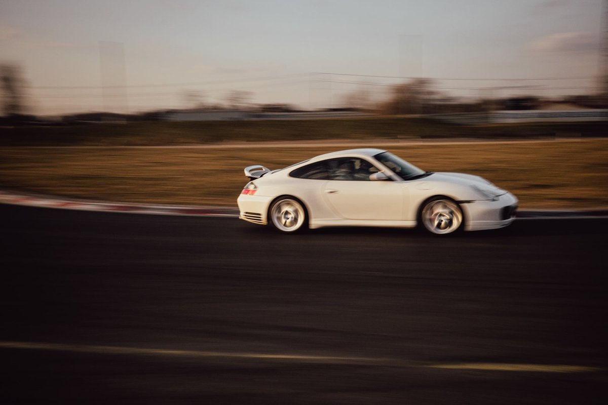 White Porsche 996.2 side profile rolling shot on track with blurred background