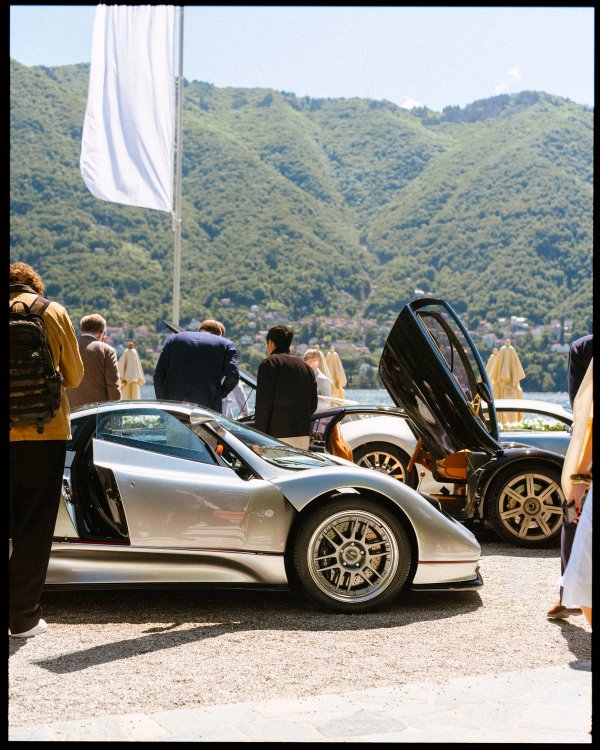 Silver Pagani Zonda and dark concept car with raised doors and a white flag, Lake Como behind