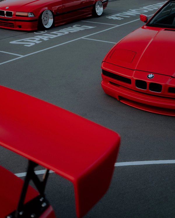 Red BMW E36 and E31 850 with red bench in foreground on parking lot with Spalding text