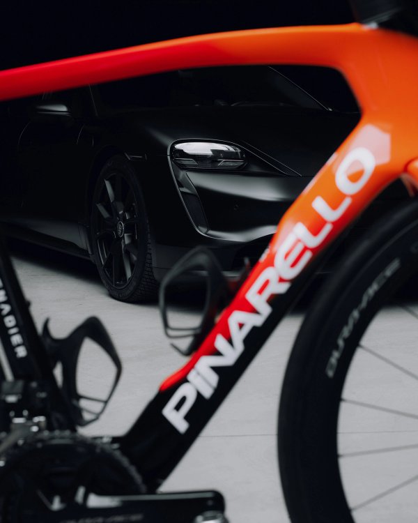 Pinarello bike frame detail in orange on black with Porsche headlight visible behind
