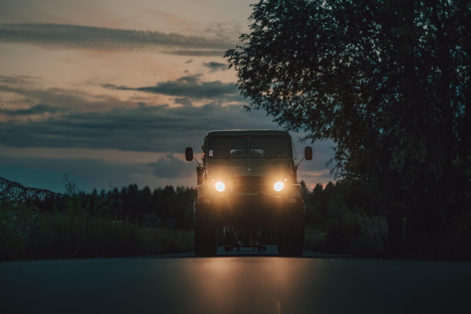 Unimog silhouette from low angle at dusk with headlights blazing on the road