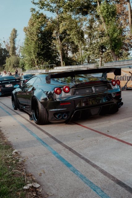 A black widebody Ferrari F430 seen from behind on the painted lines of the cycling track