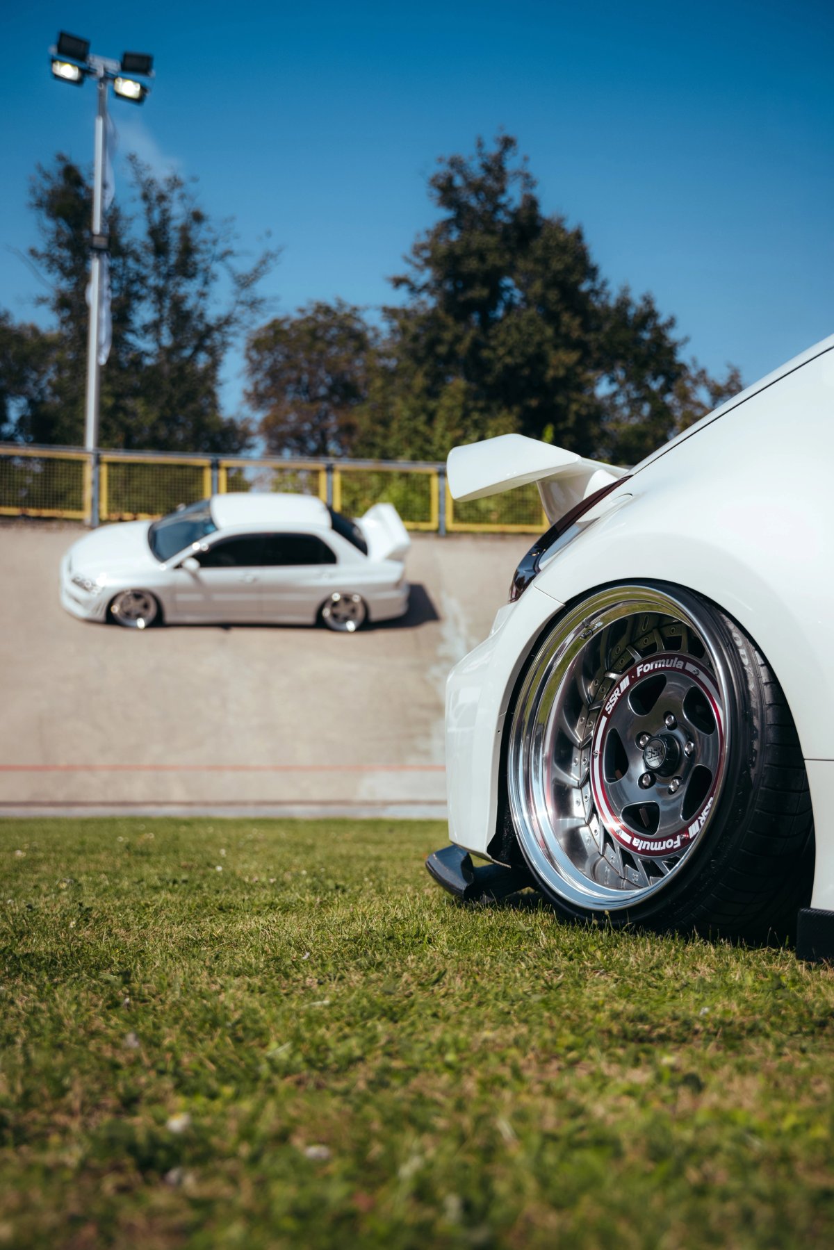 Two white cars on the velodrome banking with wheel detail in foreground on grass