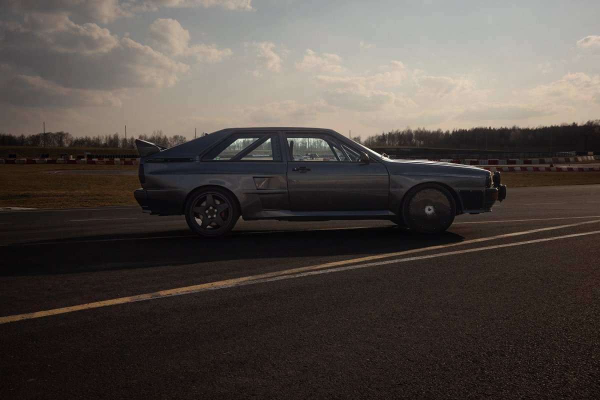 Side profile of the dark Audi ur-quattro on the track at Slomczyn showing the wide body proportions