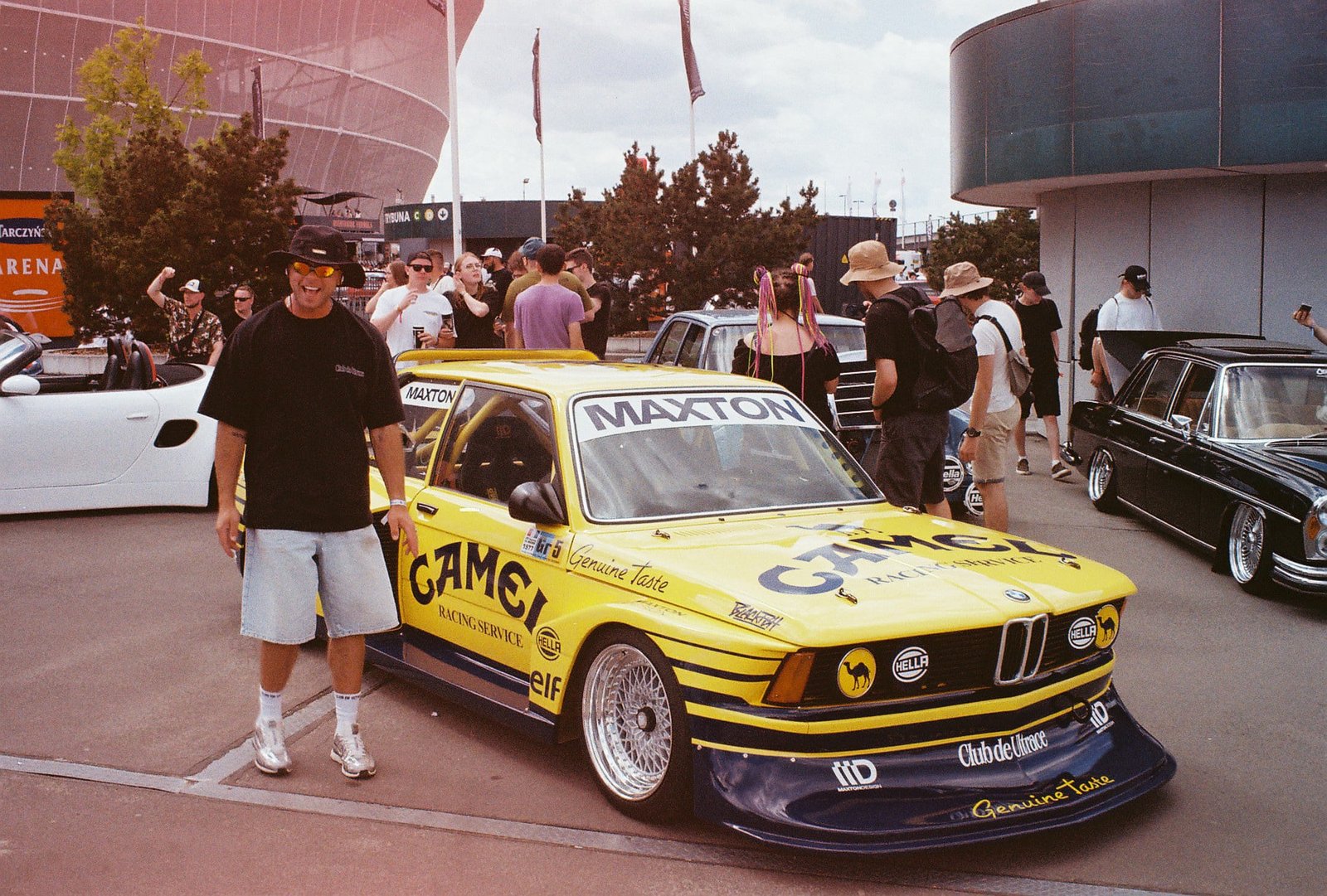 Yellow Camel-liveried BMW E21 with owner posing in front of Tarczyński Arena crowd