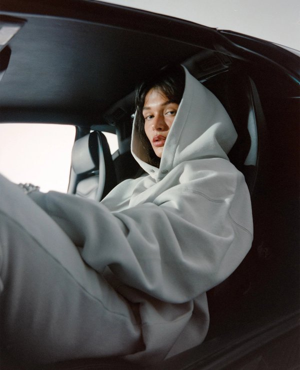 Model sitting inside a dark car with hoodie up looking through the window