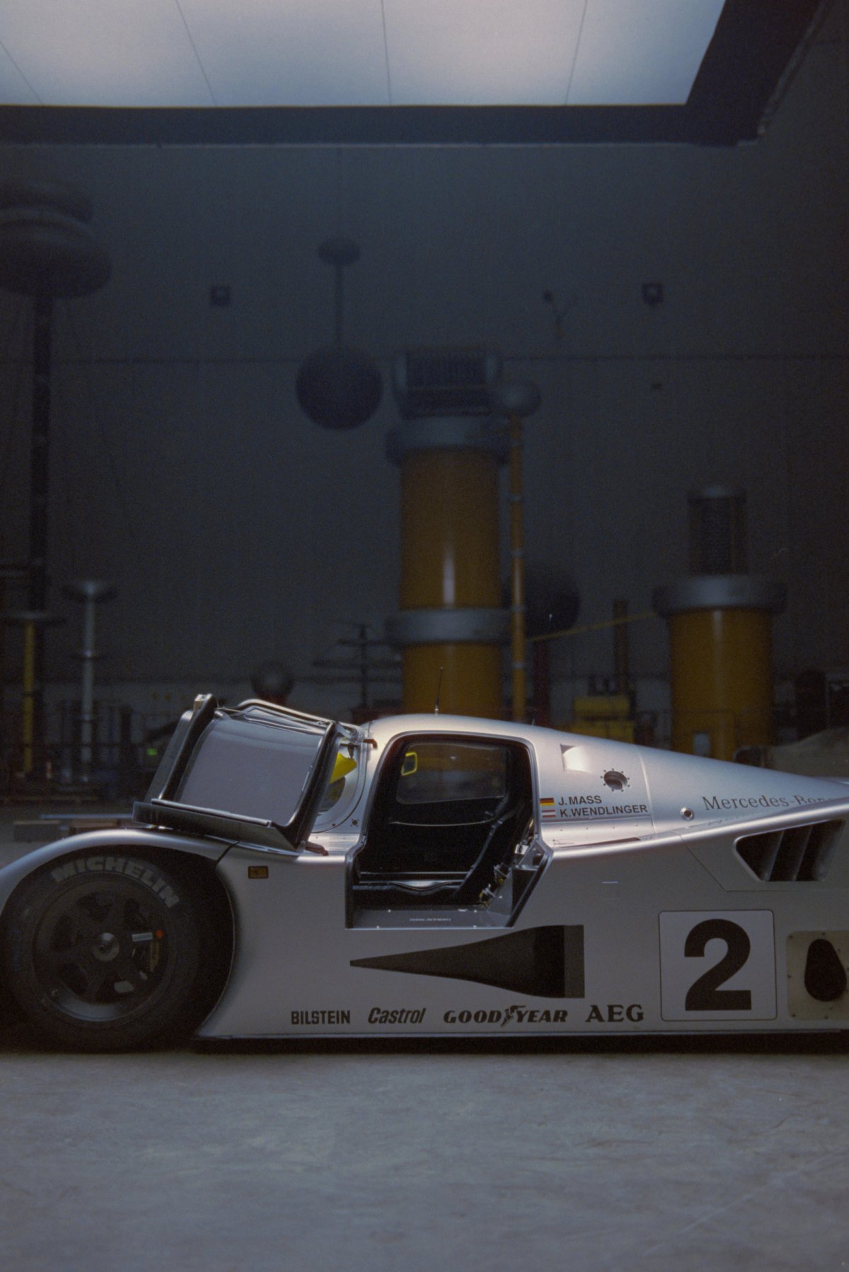 C11 side profile with body panels removed showing M119 engine exposed and yellow industrial columns behind