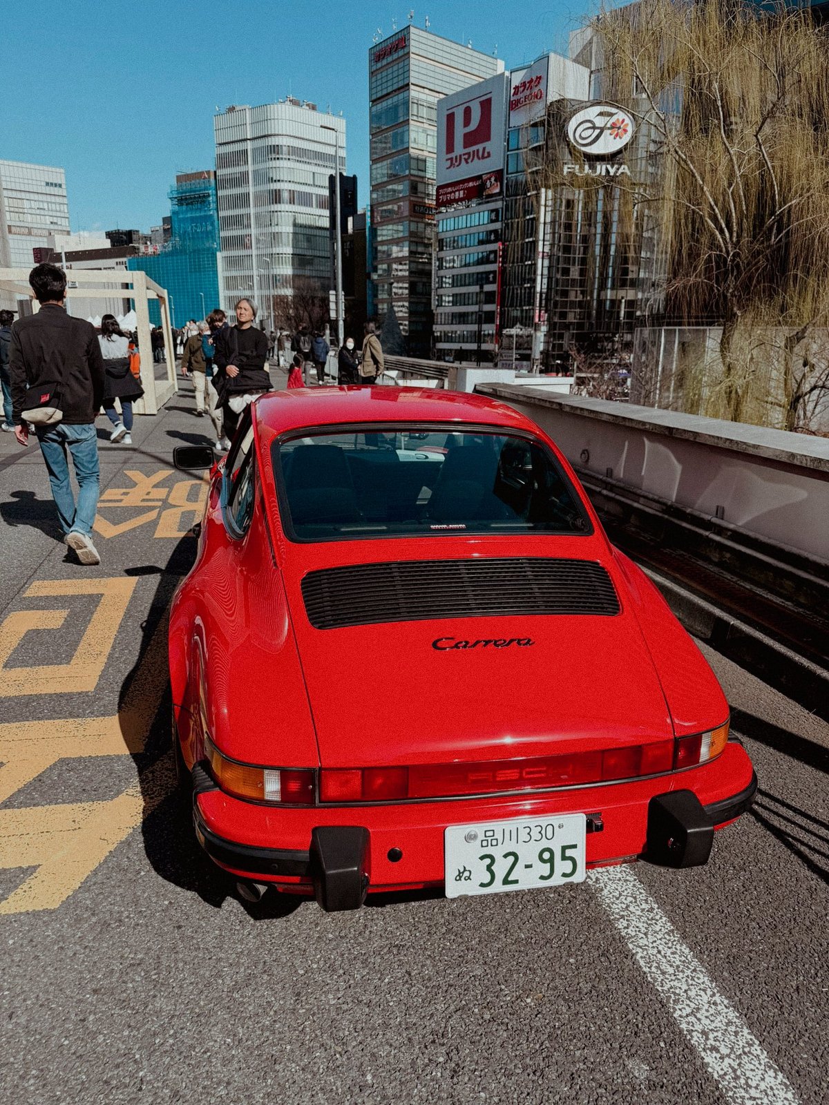 Red Porsche 911 Carrera rear view on the expressway with Fujiya sign and Ginza skyline
