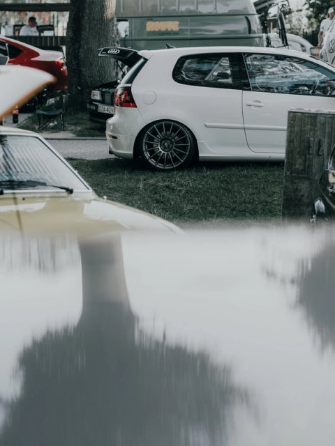 White Golf Mk5 with its tailgate up, framed between parked cars at the edge of the field