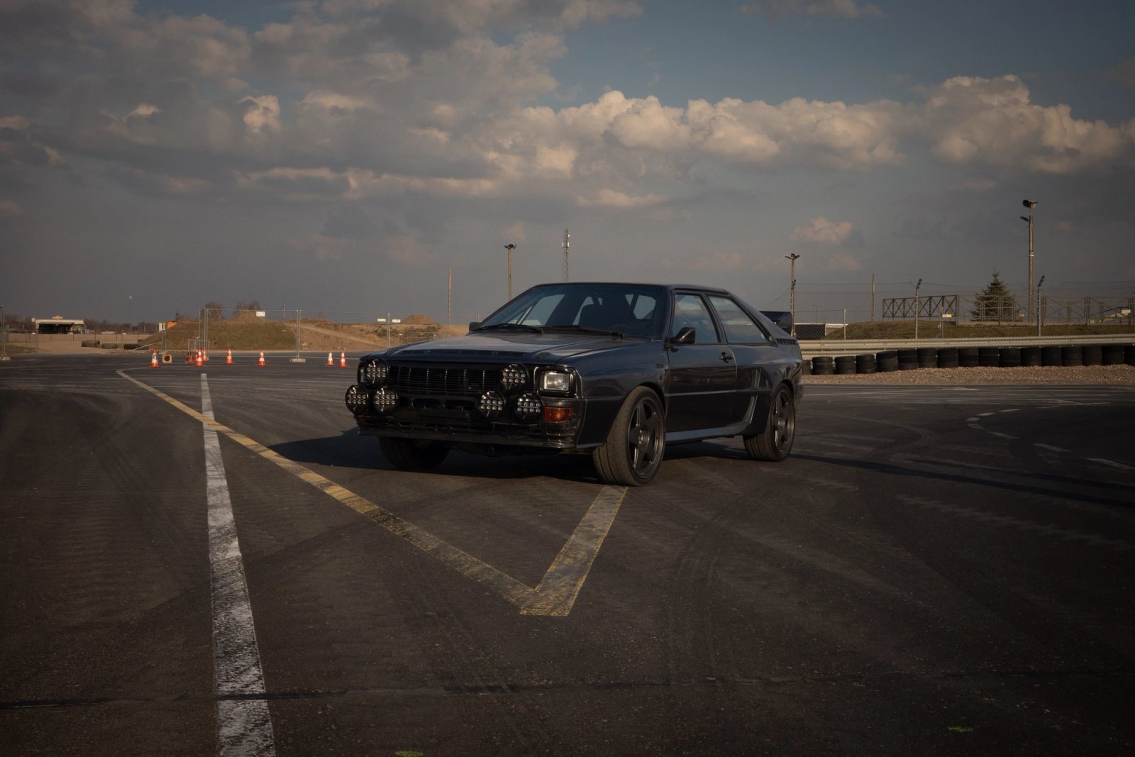 Dark Audi ur-quattro with rally light bar and aramid wide body kit standing on the track at Slomczyn at golden hour