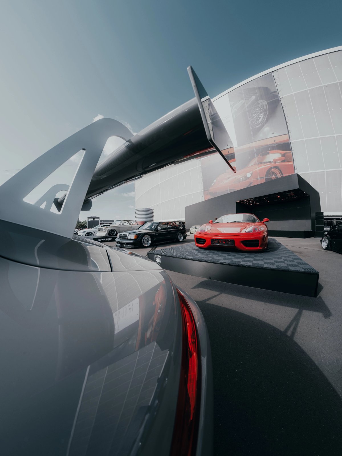 View over a car spoiler at Ultrace with red Ferrari 360 on display and LED screen behind